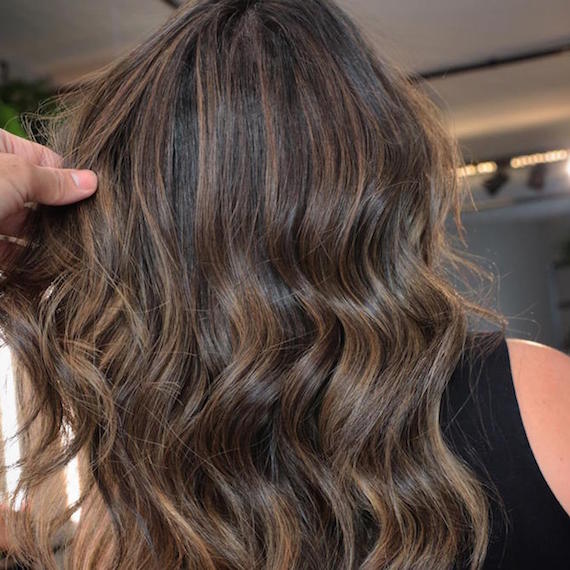 Back of woman’s head with chunky, chocolate brown highlights through long, wavy hair, created using Wella Professionals.