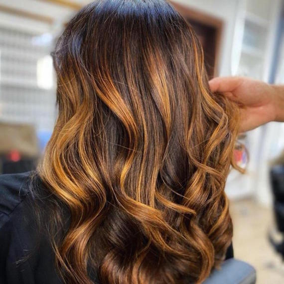 Back of woman’s head with chunky, copper highlights through long, loosely curled hair, created using Wella Professionals.