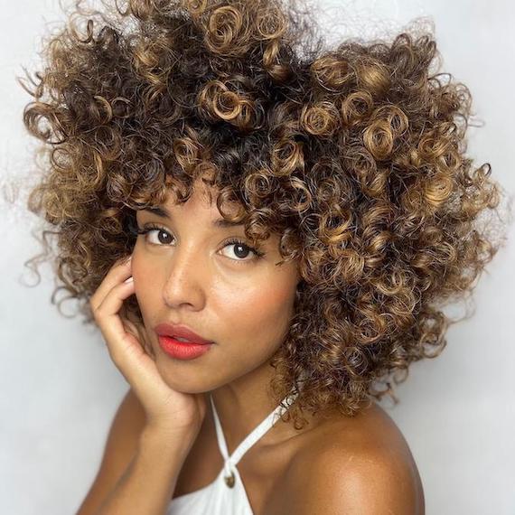 Woman facing the camera with curly, glossy, caramel hair, created using Wella Professionals.