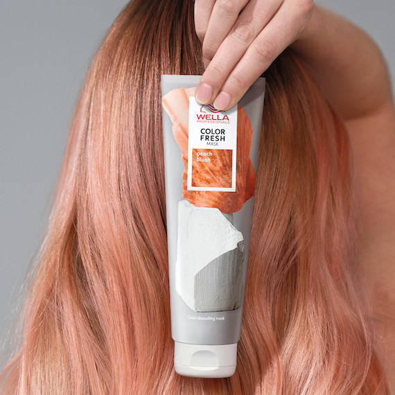 Model with light, peach blonde hair holds up a tube of the Color Fresh Mask in Peach Blush.