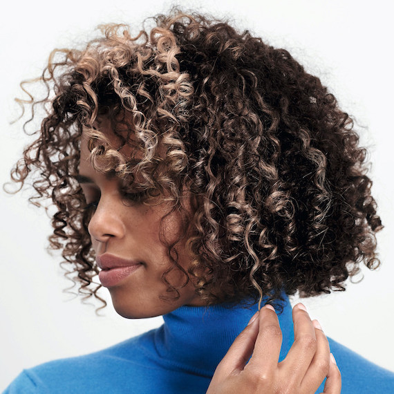 Model with dark brown, curly hair and blonde highlights looks off to the side. 