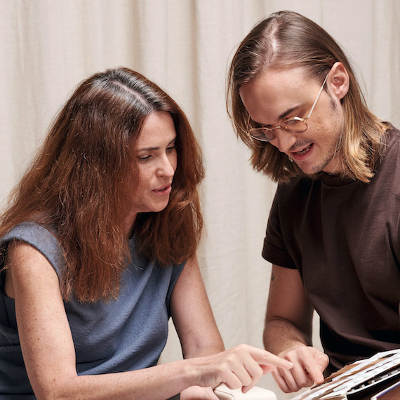 Hairdresser looks through a book of hair colour swatches with brunette client who has grey roots.