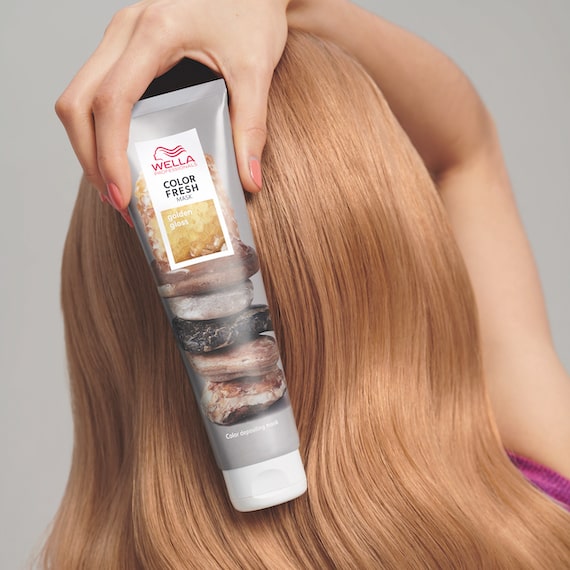Close-up of the back of a woman’s head, as she holds up a tube of the Wella Professionals Color Fresh Mask.