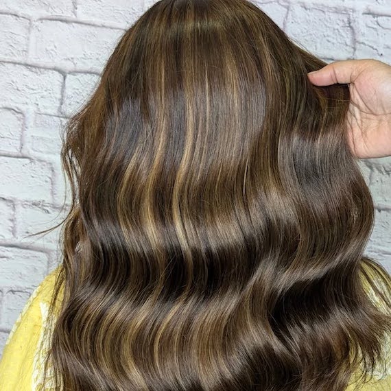 Back of model’s head with long, wavy, dark brown hair.