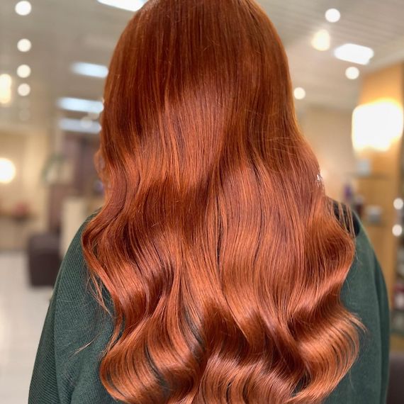 Back of model’s head with long, wavy, copper red hair.