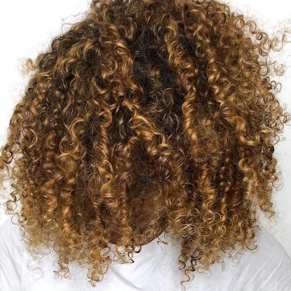 Woman with curly hair and golden highlights, created using Wella Professionals.