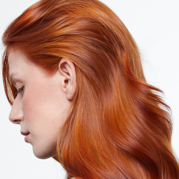 Side profile of model with long copper hair, featuring melted highlights.