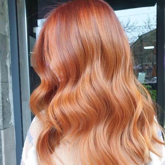 Side profile of woman with copper and strawberry blonde balayage through wavy hair, created using Wella Professionals.