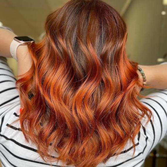 Hinterkopf einer Frau mit mittellangem, gewelltem, braunem Haar und kupferfarbenem Balayage, kreiert mit Wella Professionals.