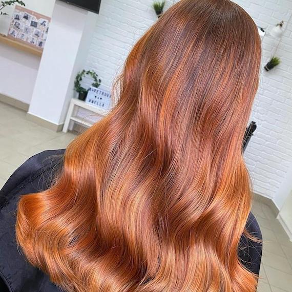 Hinterkopf einer Frau mit langem, gewelltem Haar und Kupfer-Balayage, kreiert mit Wella Professionals.