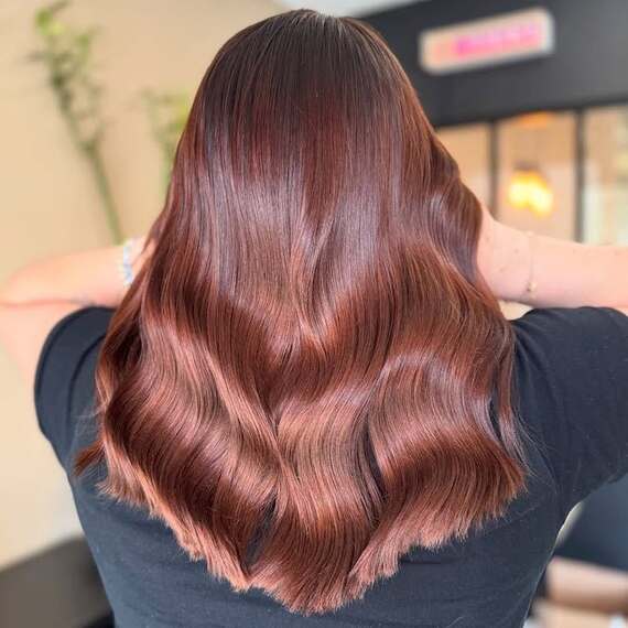 Back of model’s hair with long, glossy waves in a dark copper colour.