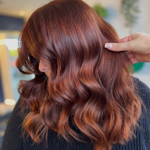 Side profile of model with long, auburn hair featuring brighter copper highlights.