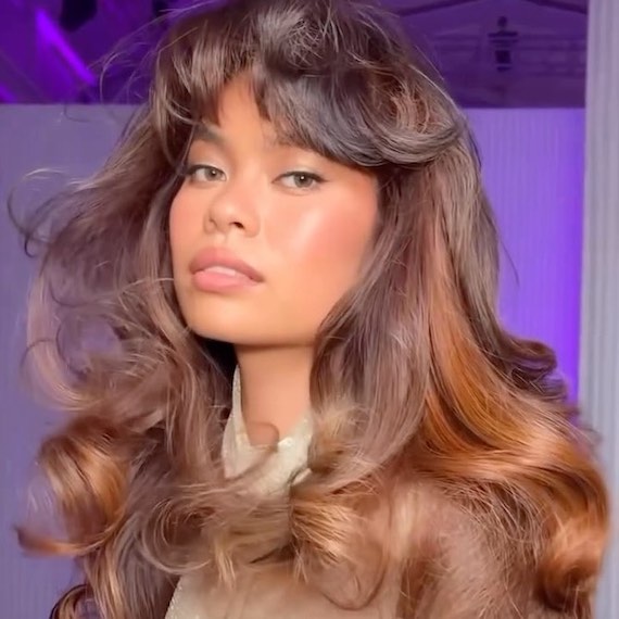 Model with dark brown hair styled in a bouncy blow-dry, featuring subtle copper highlights.