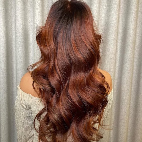 Back of model’s head with long, dark brown hair featuring auburn balayage.