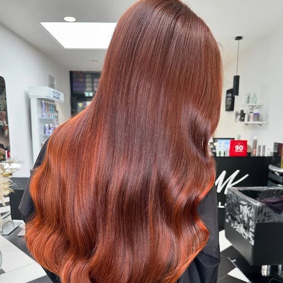 Side profile of model with long, ultra-shiny, copper brown hair.