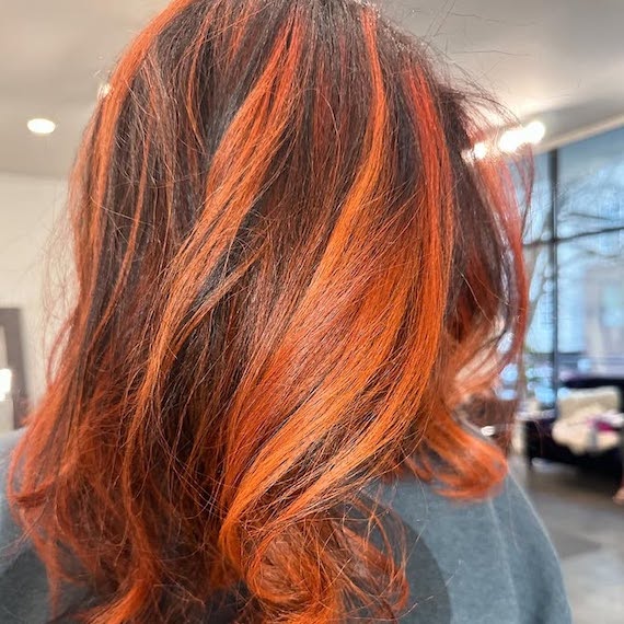 Model with dark brown hair featuring fiery copper highlights.