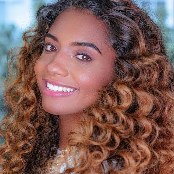 Model with long, curly, dark brown hair featuring light copper highlights.