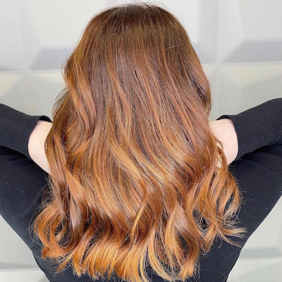 Back of woman’s head with mid-length, wavy, copper ombre hair color, created using Wella Professionals.