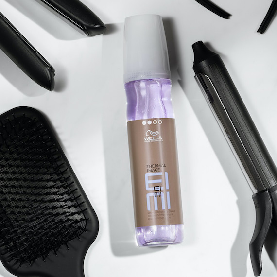 Bottle of EIMI Thermal Image heat protectant spray by Wella Professionals surrounded by styling tools