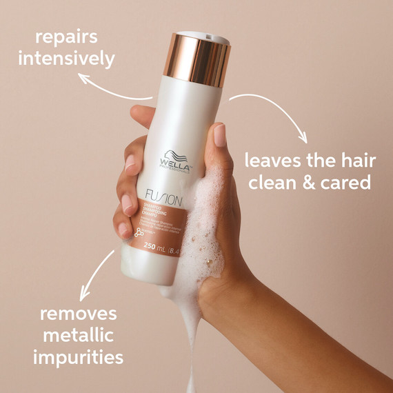 Hands holds a bottle of Fusion Intense Repair Shampoo, which removes metallic impurities and intensively repairs the hair.