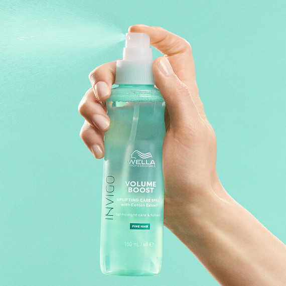 Hand holds and sprays a bottle of INVIGO Volume Boost Uplifting Care Spray.