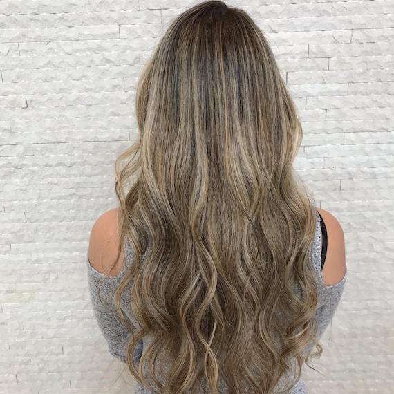 Image of the back of a woman’s head with long, dark blonde hair and multi-tonal blonde babylights. Hair is styled in long, loose waves. Look created by Wella Professionals. 