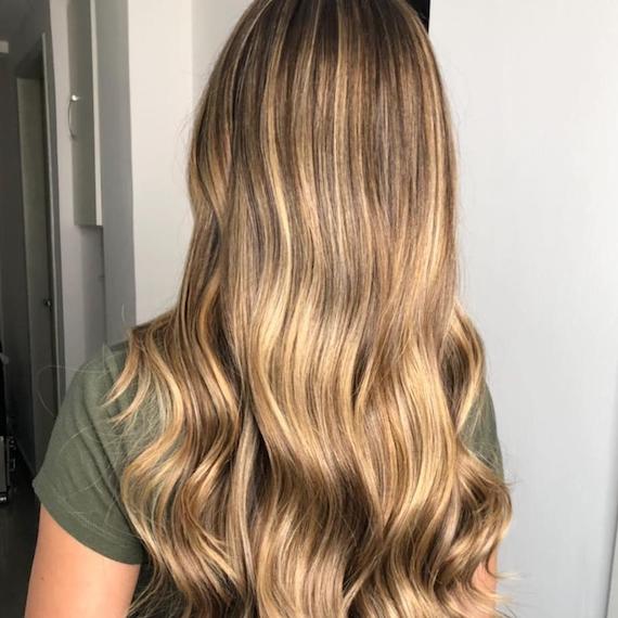 Image of the back of a woman’s head with caramel dark blonde hair, styled in long, loose waves. Look created by Wella Professionals.