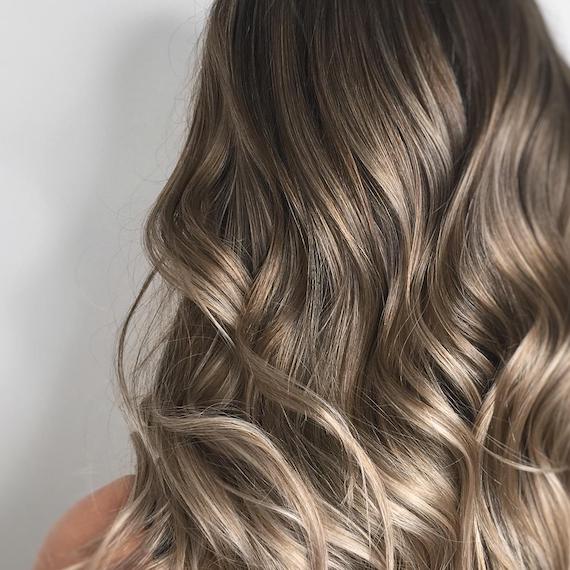 Image of the back of a woman’s head with dark blonde balayage color styled in loose waves. Look created by Wella Professionals.