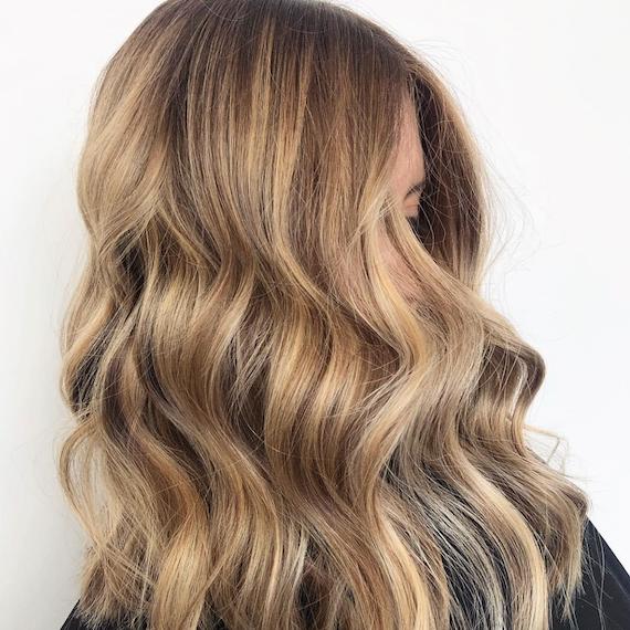 Image of a woman’s side profile with honeyed dark blonde hair color styled in loose waves. Look created by Wella Professionals.