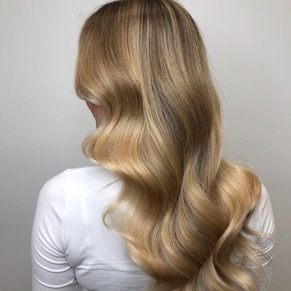 Image of the back of a woman’s head with golden dark blonde hair color styled in soft waves. Look created by Wella Professionals.