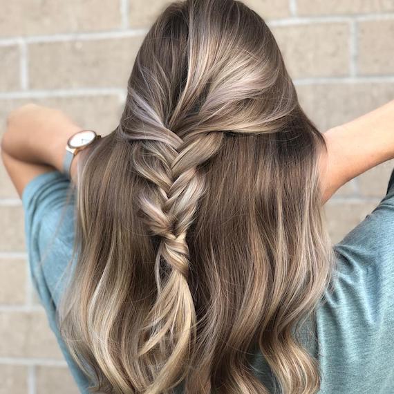 Image of the back of a woman’s head with dark blonde hair and creamy blonde highlights. Hair is styled in half-up plait with a soft wave through hair. Look created by Wella Professionals.