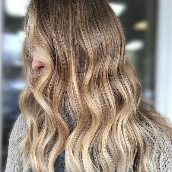 Image of side profile of a woman with buttery dark blonde hair, styled in long, loose waves. Look created by Wella Professionals.