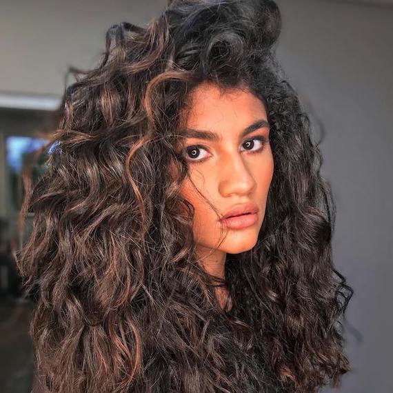 Model with curly black hair and blonde highlights.
