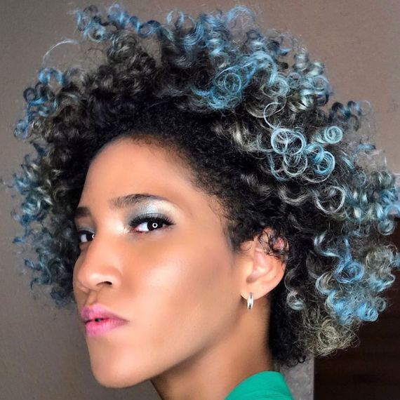 Model with short, curly brown hair with bright blue highlights running through the mid-lengths and ends.