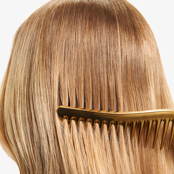 Golden comb runs through glossy, blonde hair.