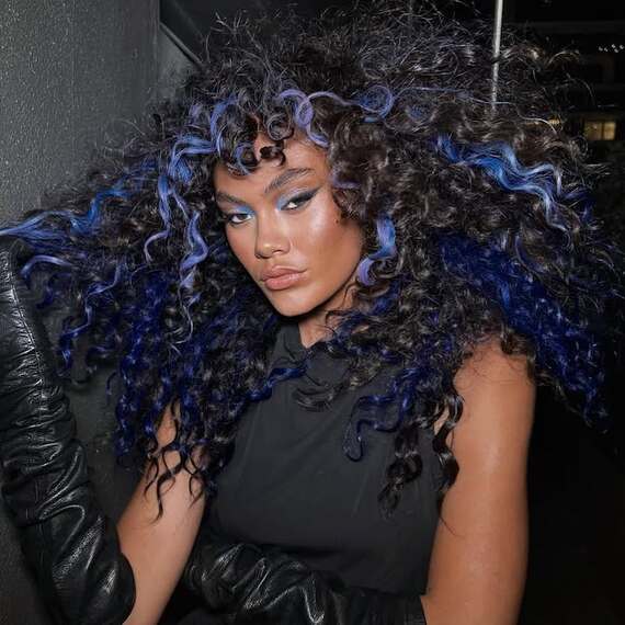 Model with black, curly hair featuring blue highlights.