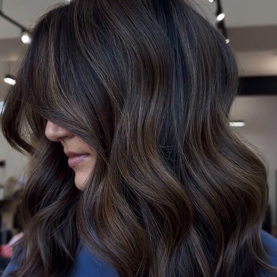 Model with dark brown hair styled in loose waves, featuring partial coffee highlights.