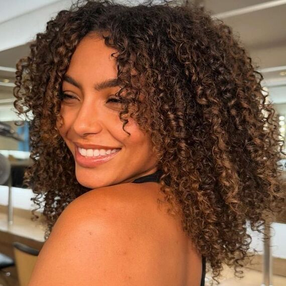 Model with chocolate brown, curly hair featuring caramel sun-kissed highlights.