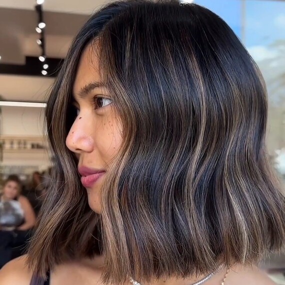 Side profile of model with shoulder-length, dark brown hair featuring sun-kissed golden highlights.