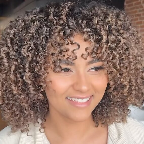 Model with dark brown, curly hair featuring cool-toned mushroom highlights.