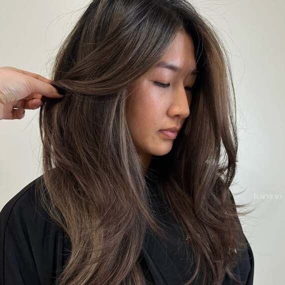 Model with long, dark hair featuring subtle caramel highlights. 