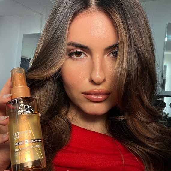 Model with dark brown, straight hair holding a bottle of ULTIMATE SMOOTH Miracle Oil Serum.