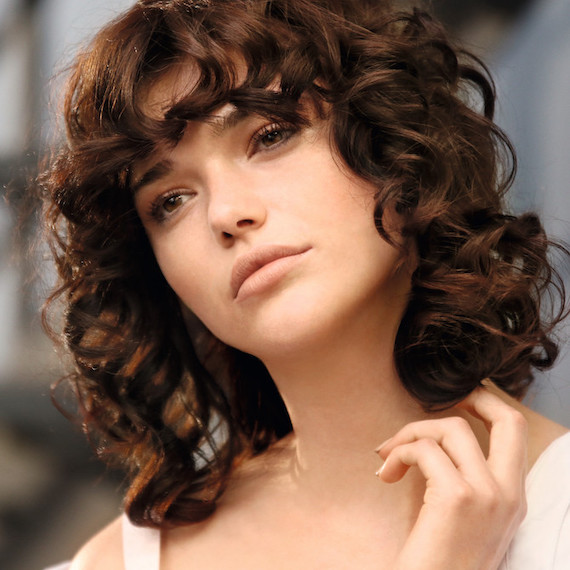 Model with dark brown, curly permed hair gazes off into the distance.