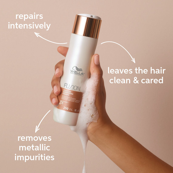 Hand holds bottle of Wella Fusion Intense Repair Shampoo with foam running down the side.