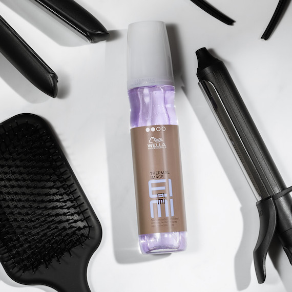 Bottle of EIMI Thermal Image and hair styling tools lie on a flat, white surface.