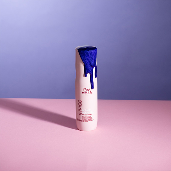 Purple shampoo spills over the side of a bottle of INVIGO Blonde Recharge Cool Blonde Shampoo.