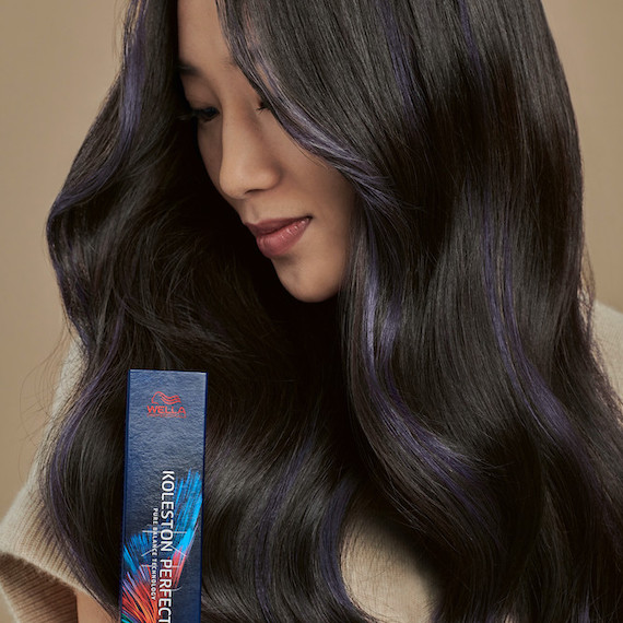 Model with long, wavy, black hair and purple highlights looks at back of Koleston Perfect hair colour.