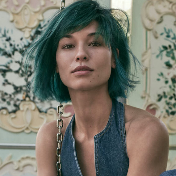 Model with green hair styled in a tousled bob looks at the camera.