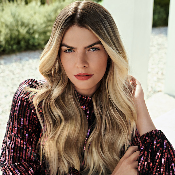 Model with long, wavy blonde highlighted hair is wearing a pink sequin clothing