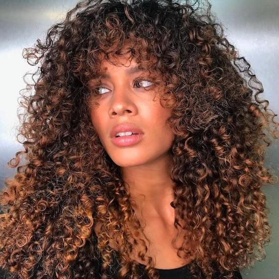 Model with chocolate brown curly hair looks to the side while facing the camera.